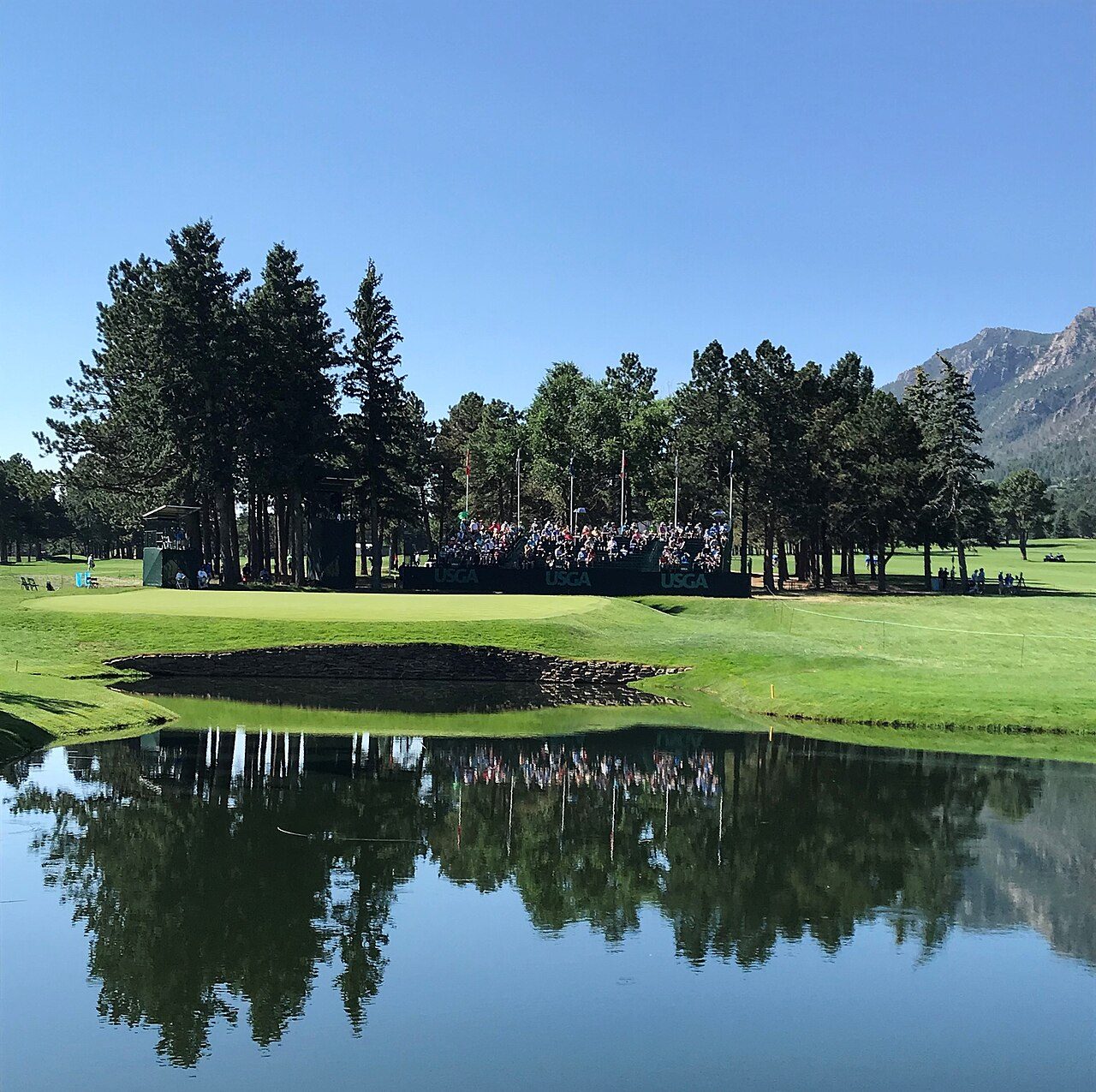 A lake reflecting pines beside a green at The Broadmoor in Colorado Springs, with the Rocky Mountain foothills behind