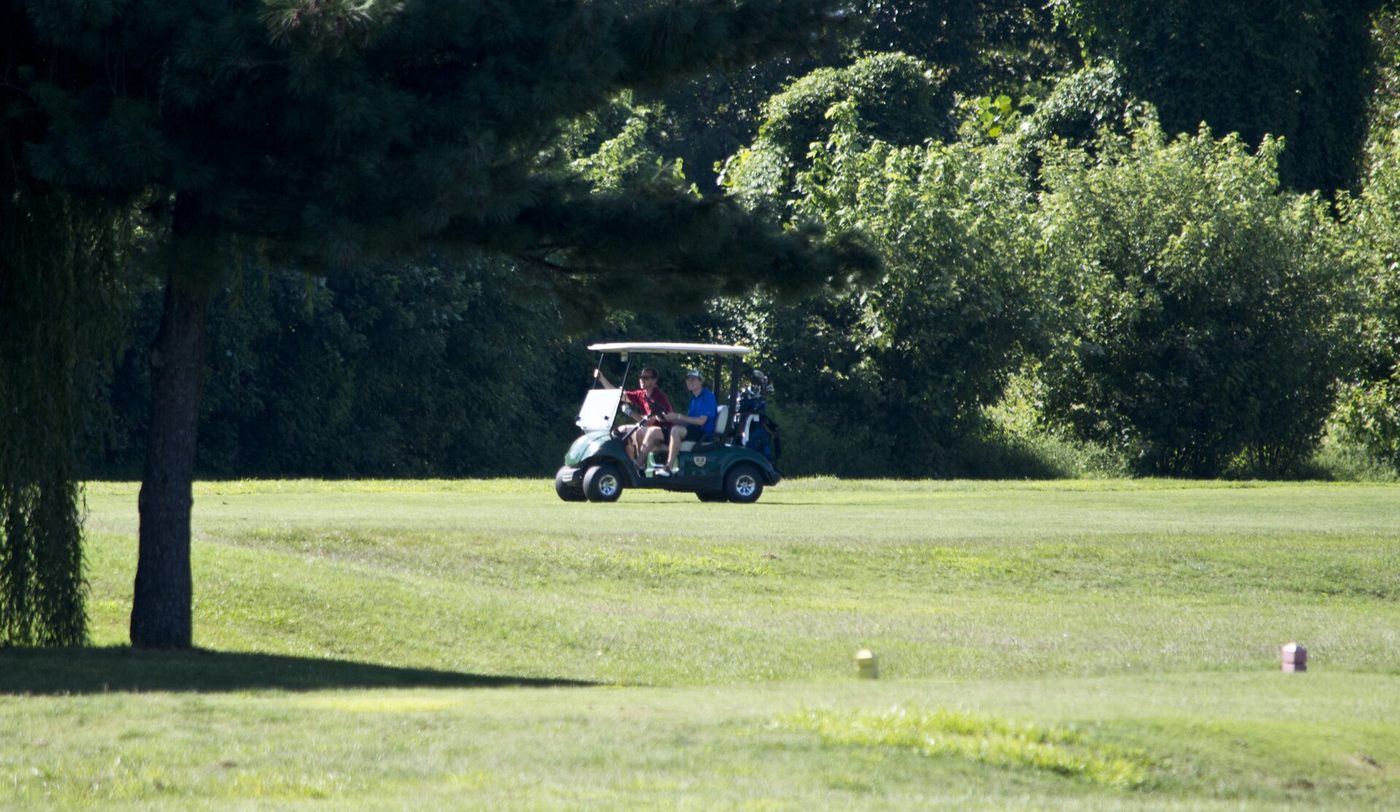 Two golfers riding a cart along a tree-lined fairway at East Potomac Park Golf Course in Washington, D.C.