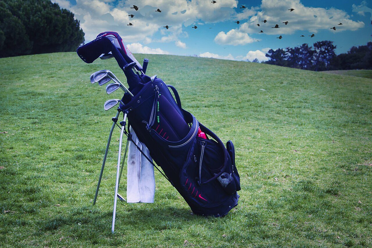A golf stand bag with irons and a hybrid resting on a grass slope
