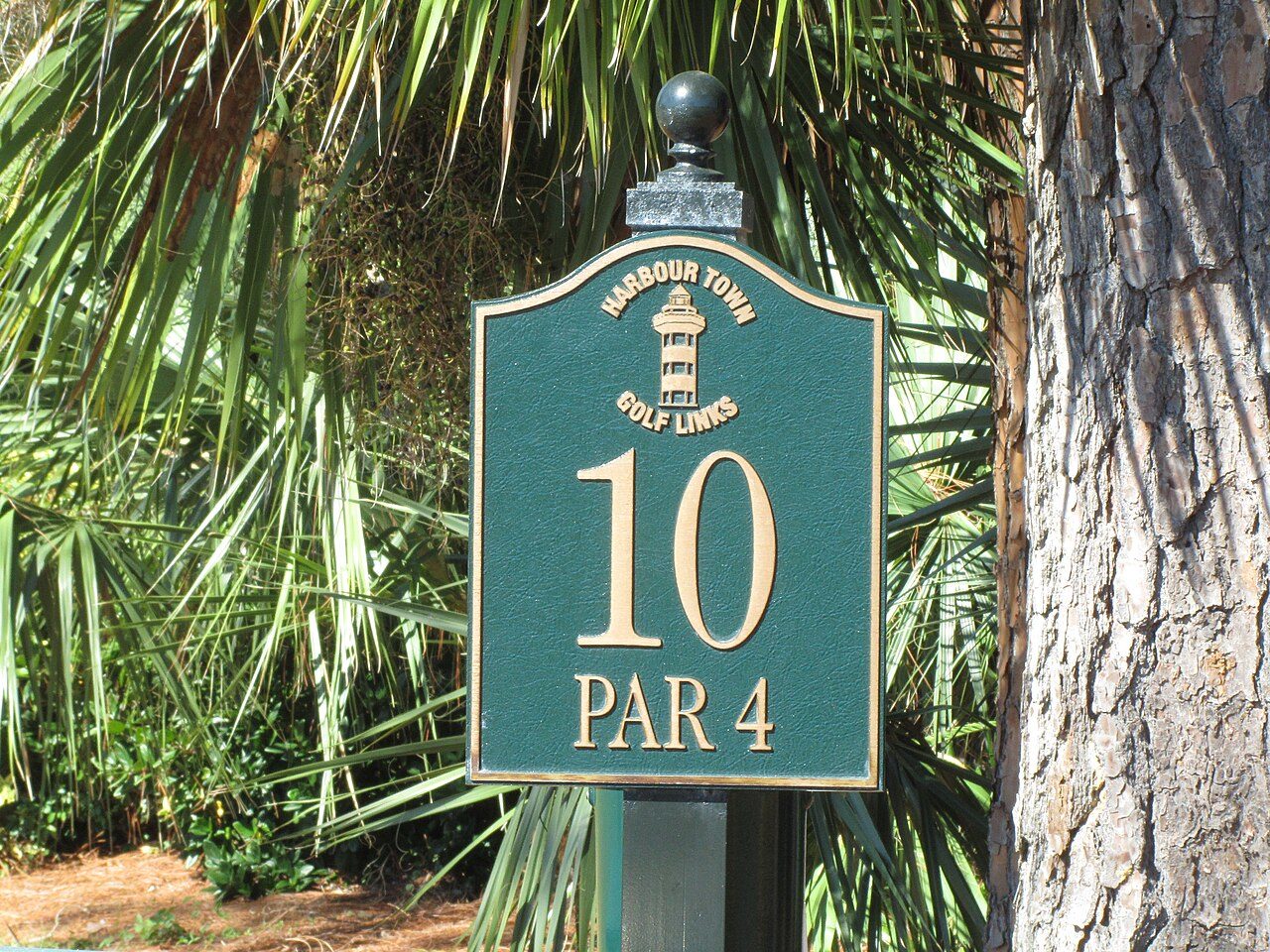 A green sign for the par-4 tenth hole at Harbour Town Golf Links, framed by palmettos