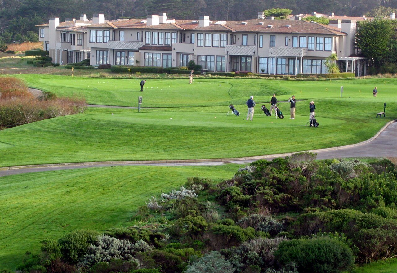 The first tee at The Links at Spanish Bay, with golfers walking toward the fairway and the inn behind
