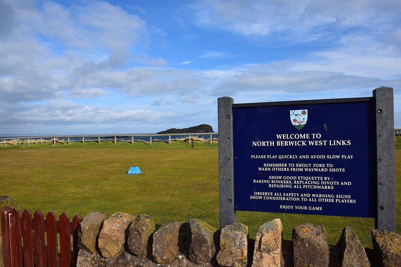 Welcome sign at North Berwick West Links, with the first tee and the Bass Rock beyond
