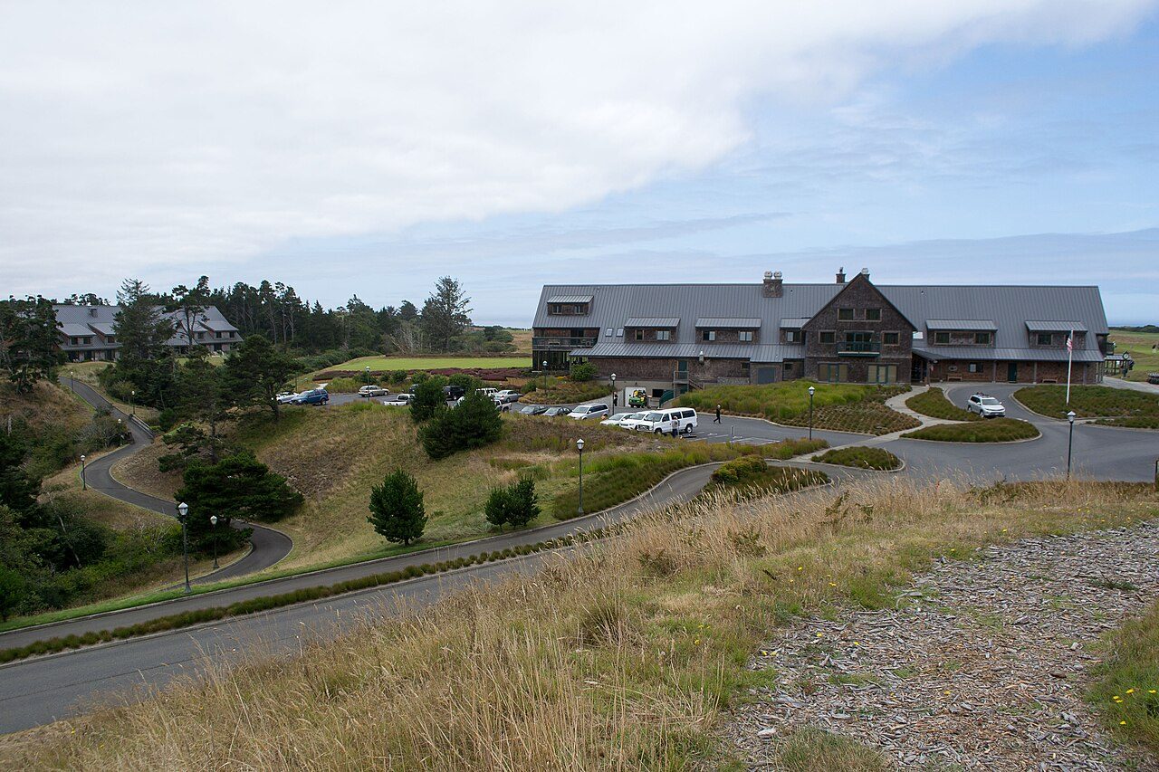 A shingled resort building above the entrance road at Bandon Dunes, with shore pines and dune grass