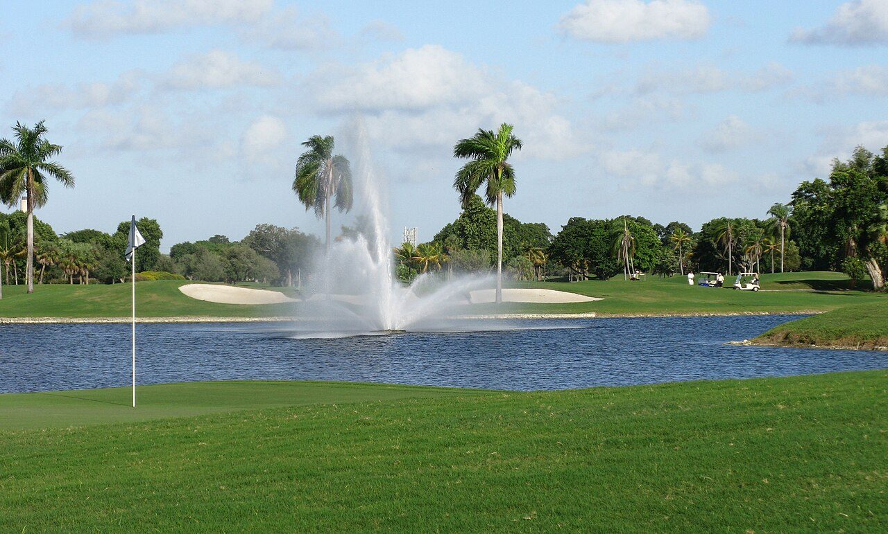 A fountain in a lake beside palms and a green at Doral golf resort in Miami
